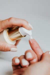 A woman applies skincare lotion from a pump bottle, showcasing manicured nails.
