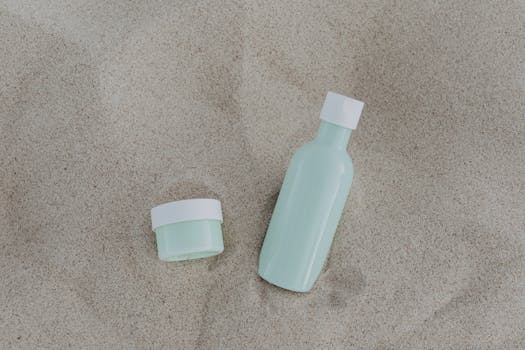 Minimalist product shot of mint green bottles on a sandy surface.